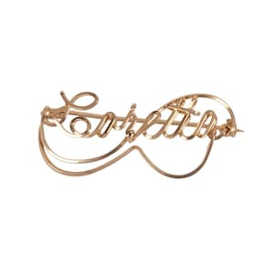 May include: Gold-toned metal brooch with the name "Carletta" written in cursive.
