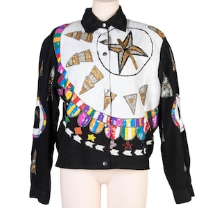 May include: A black jacket with a white sequined panel featuring a gold star and geometric shapes. The jacket has a black collar and sleeves, with colorful sequin accents and a button-up front. A unique, eye-catching piece.