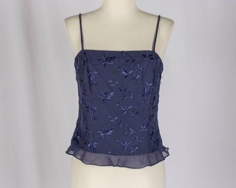 Könnte beinhalten: Ein ärmelloses Oberteil in Marineblau mit einem Blumenmuster. Das Oberteil hat einen Rüschen-Saum und einen quadratischen Ausschnitt.