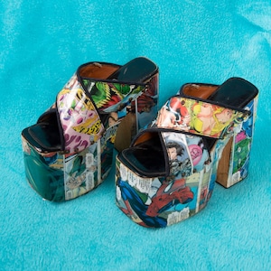May include: A pair of platform sandals with a comic book print. The sandals are black with a white and red comic book print. The sandals have a thick platform sole and a strap across the foot.