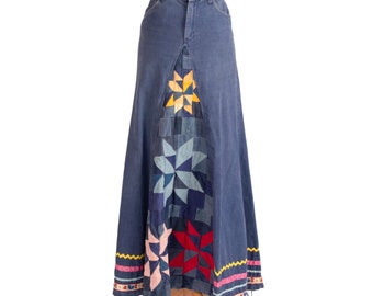 May include: A long denim skirt with a patchwork design featuring a variety of blue, pink, red, and yellow colors. The skirt has a scalloped hem and a waistband with a zipper closure.