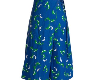 Puede incluir: Una falda azul de envoltura con estampado de delfines blancos y verdes. La falda tiene un cierre de corbata en la cintura.