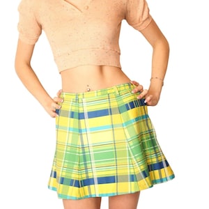 Pode incluir: Uma saia plissada xadrez em amarelo, verde e azul. A saia tem um design clássico com cintura alta e bainha na altura do joelho. A saia é combinada com um top de manga curta cor de pêssego.