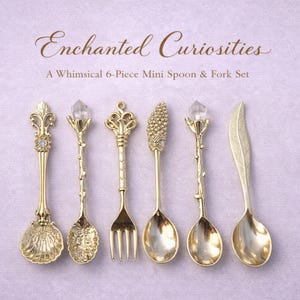 May include: A set of six gold-colored mini spoons and forks with ornate designs. The set includes spoons with crystal, leaf, and floral details, and a fork. The text "Enchanted Curiosities" and "A Whimsical 6-Piece Mini Spoon & Fork Set" are displayed.