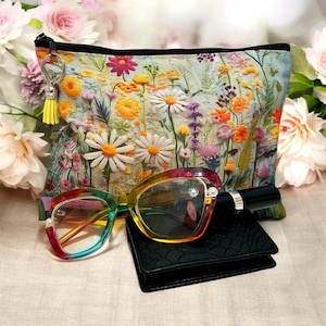 May include: A floral print cosmetic bag with a yellow tassel, rainbow-colored eyeglasses, and a black wallet. The bag features a variety of colorful flowers. The eyeglasses have a gradient of colors from blue to red.