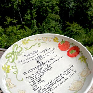 May include: A white ceramic bowl featuring a hand-painted recipe for Italian meatballs and spaghetti sauce in black cursive script. The rim is decorated with illustrations of red tomatoes, various pasta shapes, and green leafy vines.