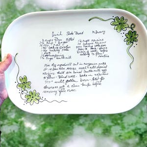 May include: A white, rectangular serving platter with a handwritten recipe for Irish Soda Bread. The recipe is in black ink, and the platter is decorated with green shamrock designs. The platter is approximately 14 inches long.