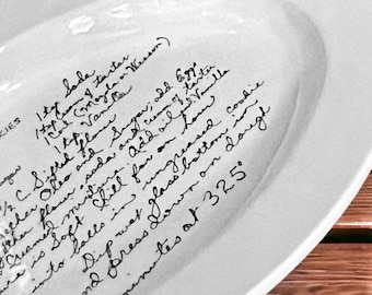 May include: White oval ceramic platter with handwritten recipe text. The recipe includes ingredients like flour, sugar, and vanilla. The text is in black ink and the platter has a slightly raised edge.