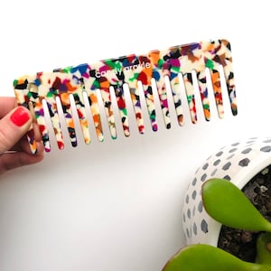 May include: A colorful comb with a white base and a multi-colored speckled pattern. The comb has the text "candy oracle" printed on it.