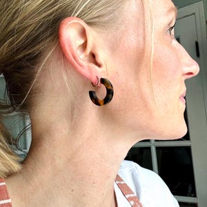 May include: A pair of brown and gold hoop earrings. The earrings are made of a tortoiseshell-like material.