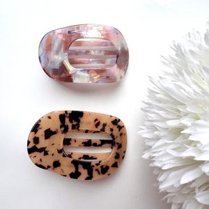 May include: Two oval-shaped hair clips with a tortoise shell and iridescent design. The clips have a comb-like design on the inside to help hold hair in place.