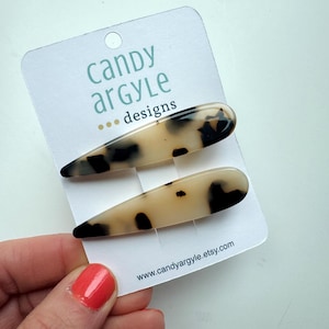 May include: Two tortoise shell hair clips on a white card with the text "Candy Argyle designs" and the website address www.candyargyle.etsy.com. The clips are teardrop-shaped with a light beige base and black spots.