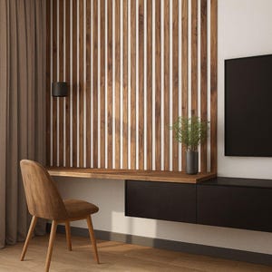 May include: A modern home office setup featuring a wooden desk, chair, and a slatted wood accent wall. The desk has a black drawer unit and a small plant in a dark vase. A black flat-screen TV is mounted on the wall.
