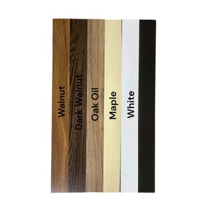 May include: A vertical display of wood samples labeled "Walnut," "Dark Walnut," "Oak Oil," "Maple," "White," and "Black." The samples showcase different wood grains and finishes, offering a variety of color options for home decor or craft projects.
