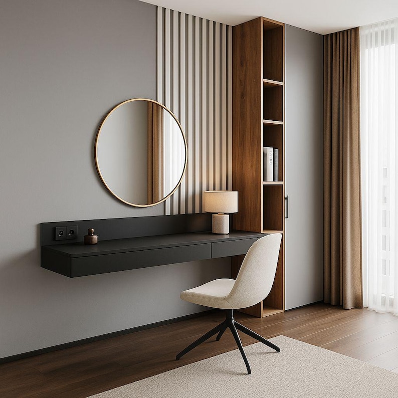 Pu&ograve; includere: Una moderna scrivania nera sospesa con uno specchio rotondo con cornice dorata, una piccola lampada e una sedia bianca. La scrivania ha due cassetti ed &egrave; montata su una parete grigia. Un mobile in legno con ripiani a destra.