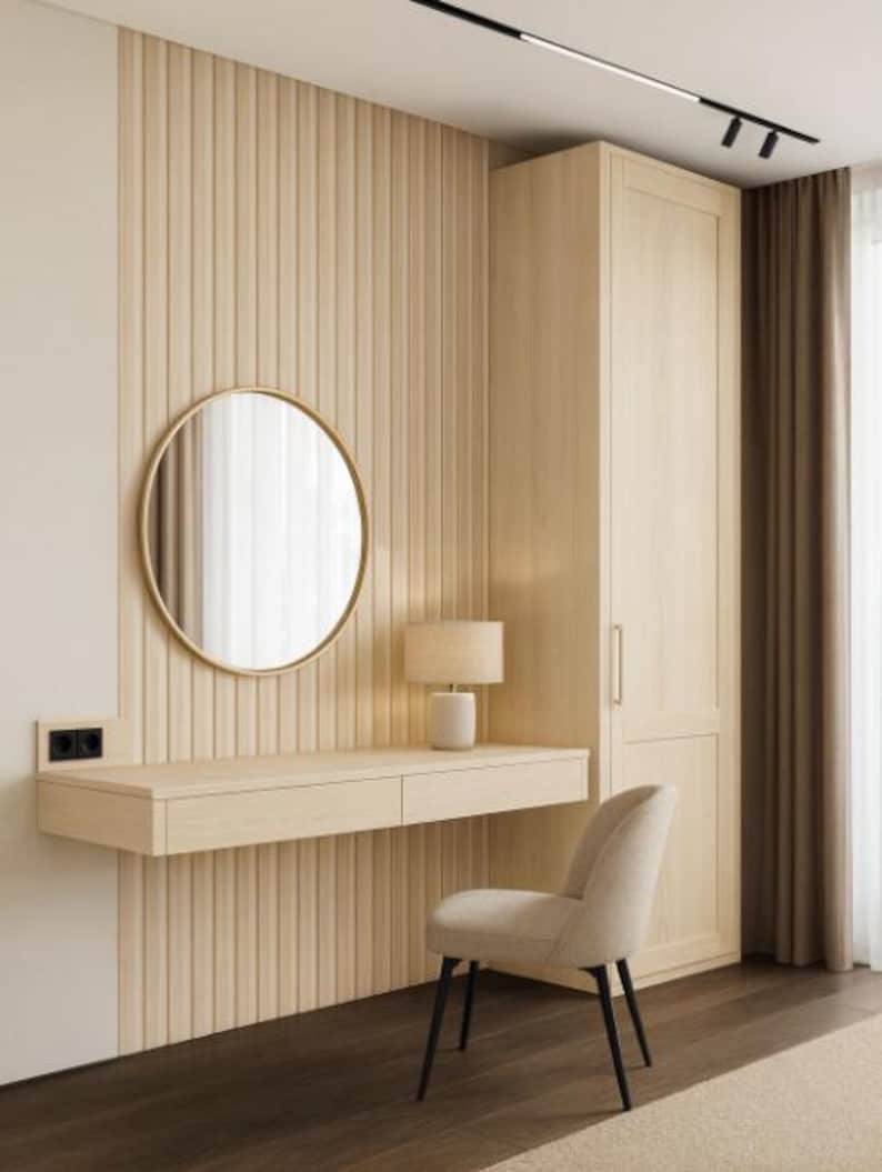 Pu&ograve; includere: Un interno di camera da letto moderno con una toeletta in legno chiaro, uno specchio rotondo e una piccola lampada. Una sedia beige imbottita con gambe nere &egrave; di fronte alla toeletta. La parete ha pannelli verticali in legno e un armadio alto &egrave; visibile.