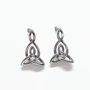 May include: A pair of silver-colored stud earrings featuring a Celtic knot design. The earrings have a three-lobed knot at the bottom, with a continuous, interwoven pattern. The earrings are displayed on a white background.