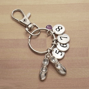 May include: Silver key chain with a purple gem, a silver charm with the number 8, a silver charm with the number 7, a silver charm with the number 6, a silver charm with the number 5, and two silver charms shaped like ballet shoes.