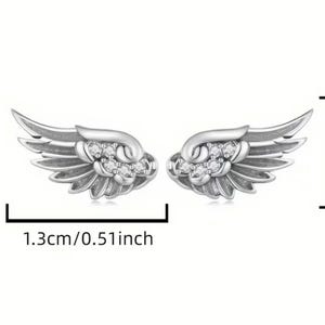Może przedstawiać: Para kolczyk&oacute;w w kształcie skrzydeł w kolorze srebrnym z osadzonymi przezroczystymi kamieniami. Kolczyki mają 1,3 cm szerokości i 0,6 cm wysokości, co wskazują czarne linie pomiarowe i etykiety tekstowe widoczne na obrazie.