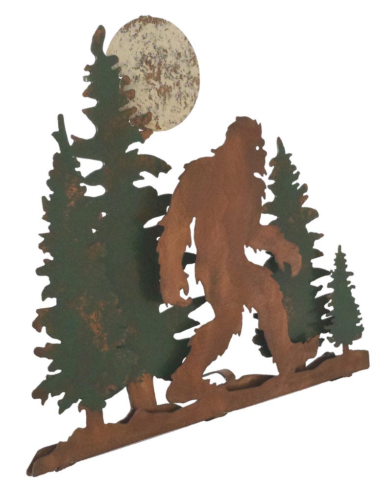 May include: Metal wall art featuring a silhouette of Bigfoot walking through a forest under a full moon. The art is painted in shades of brown, green, and white.
