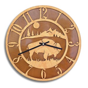 May include: A wooden wall clock with a brown background and a silhouette of a bison in a forest scene. The clock face has Roman numerals and a black hour and minute hand.