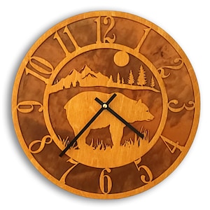 May include: A wooden clock with a brown bear silhouette and a mountain scene. The clock face has Roman numerals and a black hour and minute hand.