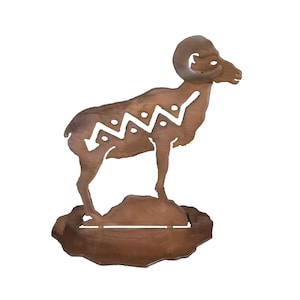 May include: A brown metal sculpture of a ram standing on a small rock. The ram has large curved horns and a decorative white zigzag pattern on its side. The sculpture is a rustic, decorative item.