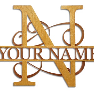 May include: Wooden sign with the letter "N" in a decorative font, with a horizontal bar that reads "YOUR NAME". The letter "N" is split by the bar, with the top half of the letter above the bar and the bottom half below the bar. The sign is made of natural wood with a light brown finish.