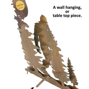 May include: A metal wall hanging or table top piece depicting a forest scene with three trees. The piece has a sawtooth hanger on the back and a stand that can be bent out for table use. The piece is made by Crooks Designs.