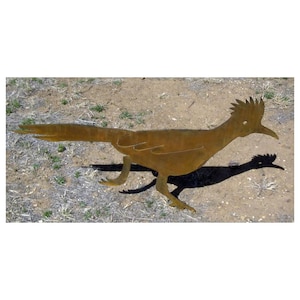 May include: A rusty metal silhouette of a roadrunner bird. The bird is standing on a dirt ground with some grass.