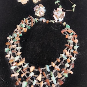 May include: A multi-strand necklace made of iridescent shell pieces and small clear beads. The necklace is paired with a set of matching earrings and a bracelet.
