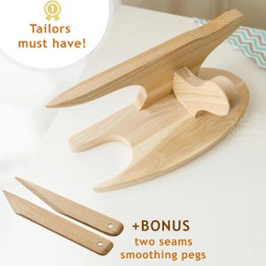 Può includere: Un cuscinetto da sarto in legno con due lisciatori per cuciture in legno. Il cuscinetto è di colore marrone chiaro e ha una forma unica. I lisciatori sono anch'essi di colore marrone chiaro e hanno una finitura liscia.