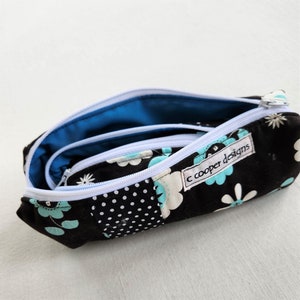May include: A black zippered pencil case with a white zipper and a blue and white floral pattern. The case has a label that reads "c cooper designs".