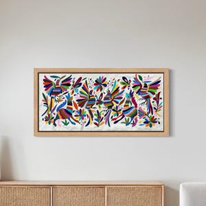 Op de afbeelding: Een ingelijst kunstwerk met een levendig, kleurrijk ontwerp van abstracte vormen en figuren. Het kunstwerk wordt tentoongesteld boven een houten kast in een moderne woonkamer. De kamer heeft een stenen muur en een dakraam.