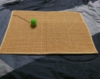 May include: A beige cat scratching post with a green pom-pom toy attached to a string.