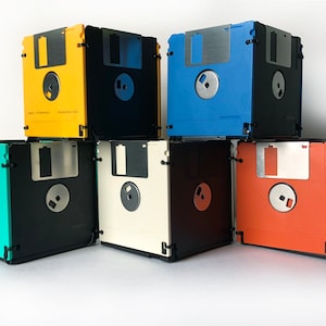 Staked simple 5-sided containers made of 3.5 inch floppy disks. Each disk is made of two disks in the same color and 3 black disks. Shown here: yellow, blue, orange, white, and seam foam green. The disks are held together with nylon cable ties.