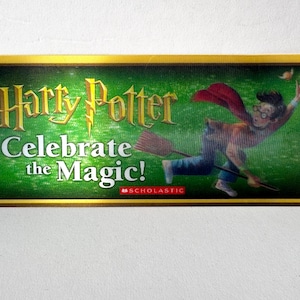 May include: Rectangular sign with a gold border featuring the words "Harry Potter Celebrate the Magic!" and an illustration of Harry Potter on a broomstick. The Scholastic logo is in the bottom right corner.