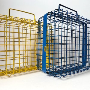 May include: Two wire metal baskets, one yellow and one blue, with rectangular shapes and handles. The yellow basket is on the left, and the blue basket is on the right. The baskets are made of a grid of metal wires.