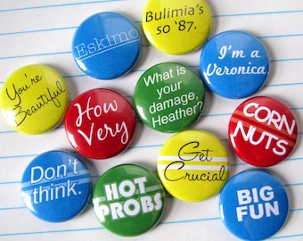 May include: Ten round button pins with various colors and text. The text on the pins includes "You're Beautiful", "Eskimo", "Bulimia's so '87.", "I'm a Veronica", "What is your damage, Heather?", "How Very", "Don't think.", "Get Crucial", "HOT PROBS", "CORN NUTS", and "BIG FUN".