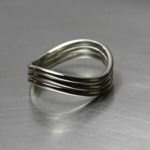 May include: A silver ring with three bands that are twisted together. The ring is smooth and shiny.