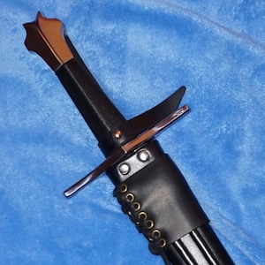 May include: A black sword with a silver crossguard and a decorative pommel. The handle is wrapped in black material, and the scabbard is black with a leather sheath. The sword is angled diagonally against a blue background.
