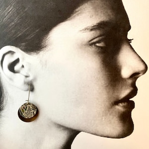 May include: A pair of gold hoop earrings with a floral pattern on the front. The earrings are made of metal and have a simple design.