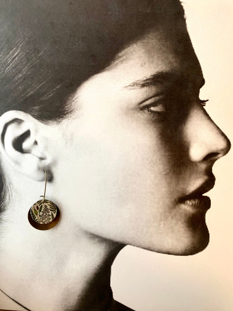 May include: A pair of gold hoop earrings with a floral pattern on the front. The earrings are made of metal and have a simple design.