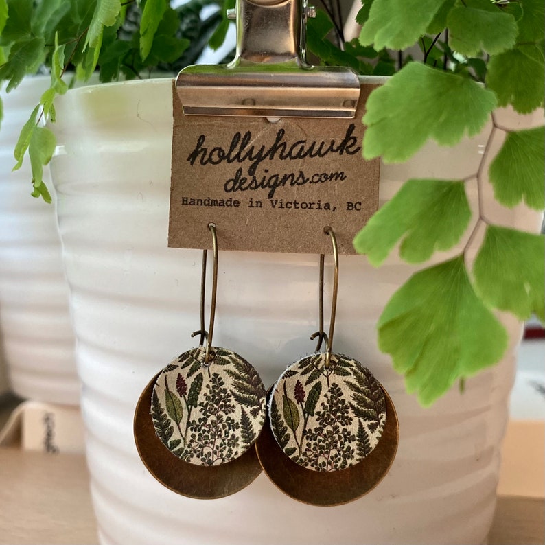 May include: A pair of brass earrings with a floral pattern on the front. The earrings are handmade in Victoria, BC by hollyhawkdesigns.com.