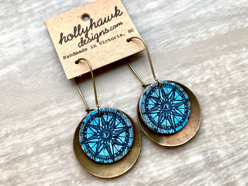 May include: A pair of dangle earrings with a blue compass design on a brass background. The earrings are handmade in Victoria, BC.