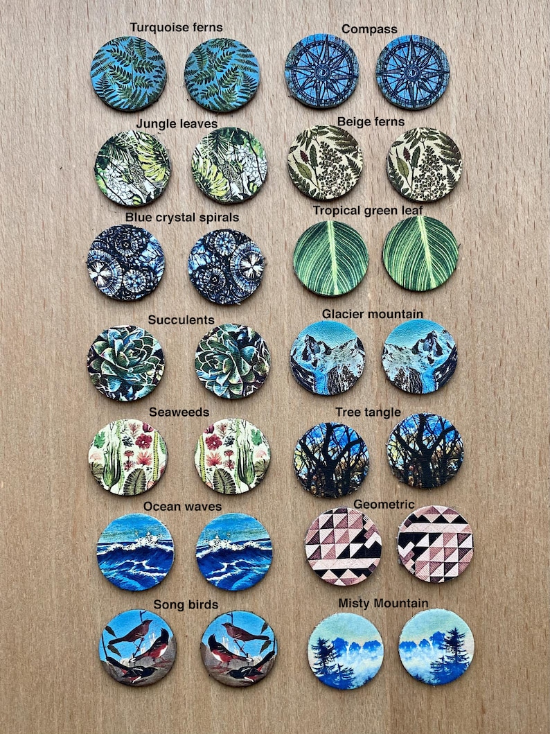May include: A set of 16 round cork coasters with various nature-inspired designs. The designs include turquoise ferns, compass, jungle leaves, beige ferns, tropical green leaf, blue crystal spirals, glacier mountain, succulents, seaweeds, tree tangle, ocean waves, geometric, song birds, and misty mountain.
