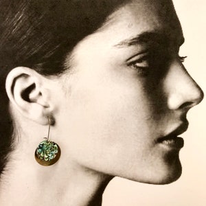 May include: A pair of silver dangle earrings with a green and blue floral design. The earrings are made of metal and have a simple, elegant design.