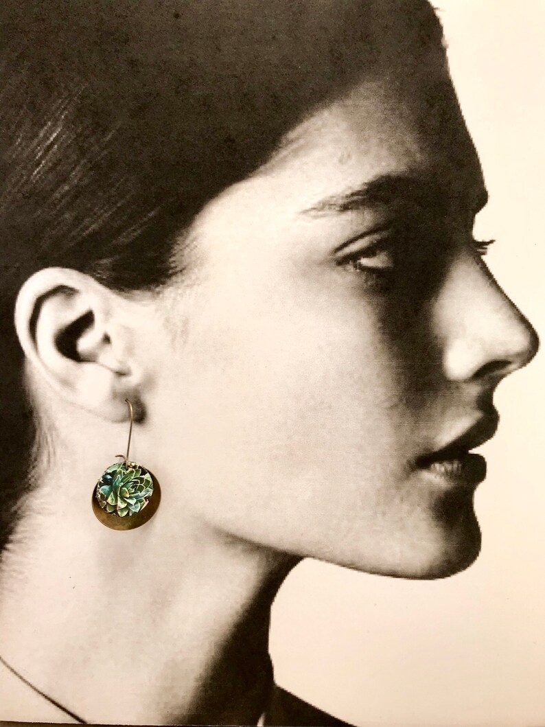 May include: A pair of silver dangle earrings with a green and blue floral design. The earrings are made of metal and have a simple, elegant design.