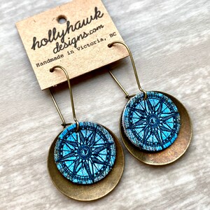 May include: A pair of dangle earrings with a blue compass design on a brass background. The earrings are handmade in Victoria, BC.
