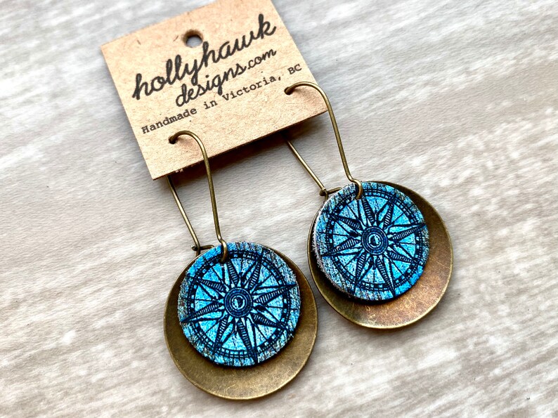 May include: A pair of dangle earrings with a blue compass design on a brass background. The earrings are handmade in Victoria, BC.